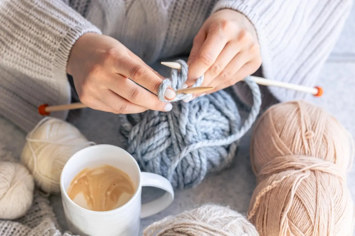 Nahaufnahme einer Frau, die mit grauem Garn strickt.