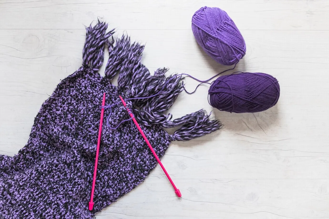 Violettes Garn und Stricknadeln auf einem Wollschal.
